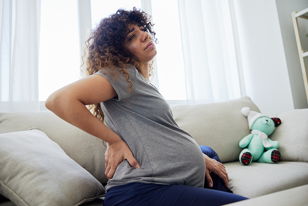 5 PT techniques that can improve SI joint pain while pregnant pregnant woman sitting on the couch lower back pai 2023 12 19 07 01 11 utc 1 5 pt techniques that can improve si joint pain while pregnant ssor